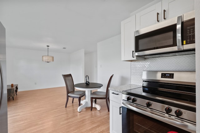 kitchen with pendant lighting, white cabinets, decorative backsplash, appliances with stainless steel finishes, and light hardwood / wood-style floors