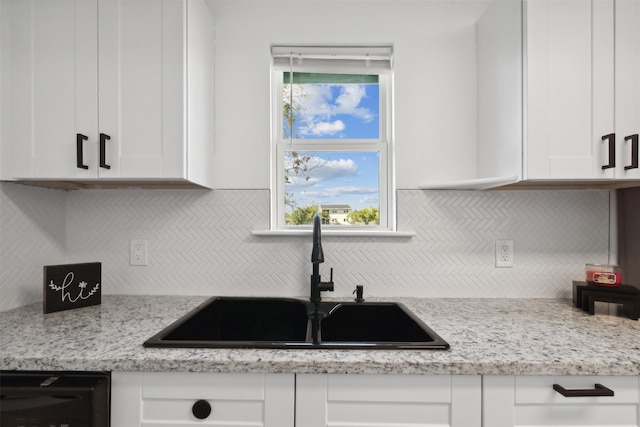 kitchen featuring white cabinets, tasteful backsplash, light stone countertops, and sink