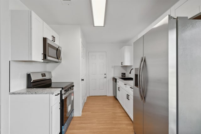 kitchen with sink, stainless steel appliances, white cabinetry, and light hardwood / wood-style flooring