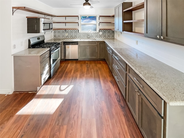 kitchen with light stone counters, ceiling fan, sink, stainless steel appliances, and dark hardwood / wood-style flooring