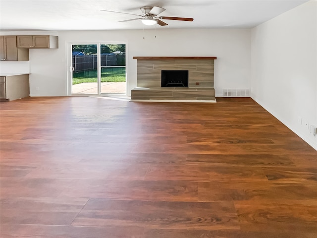 unfurnished living room with ceiling fan, a tile fireplace, and dark wood-type flooring