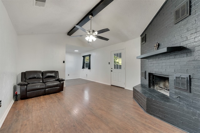 living room with a textured ceiling, dark wood-type flooring, a fireplace, vaulted ceiling with beams, and ceiling fan