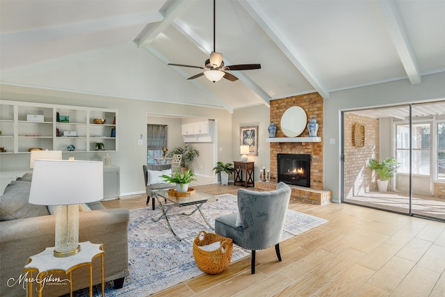 living room with ceiling fan, beam ceiling, a brick fireplace, high vaulted ceiling, and light hardwood / wood-style floors