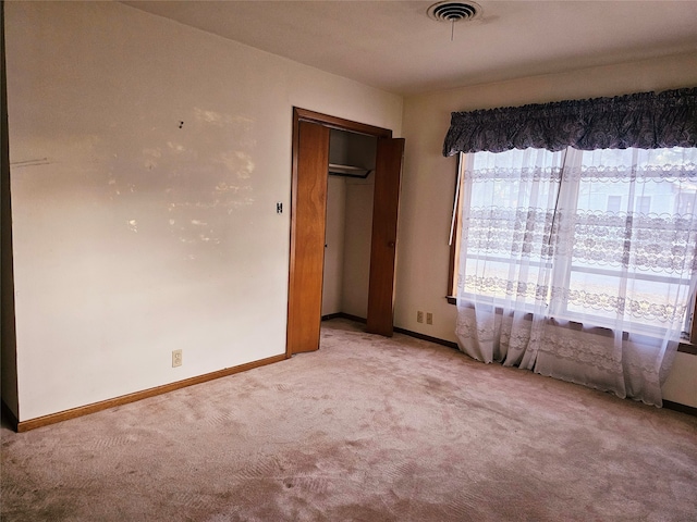 unfurnished bedroom featuring multiple windows, light carpet, and a closet