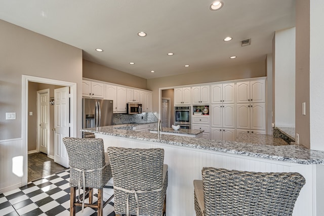 kitchen featuring white cabinetry, stainless steel appliances, light stone counters, tasteful backsplash, and kitchen peninsula