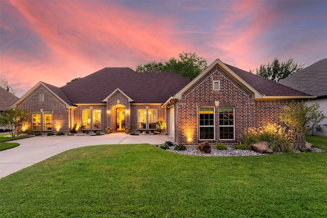 view of front of house with a shingled roof, concrete driveway, brick siding, and a yard