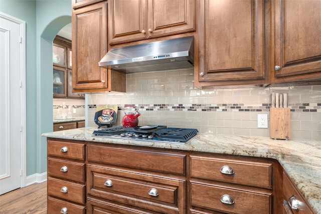 kitchen with light stone counters, decorative backsplash, stainless steel gas stovetop, and light wood-type flooring