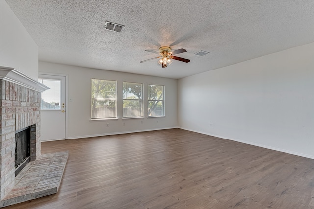 unfurnished living room featuring a healthy amount of sunlight, dark wood-type flooring, ceiling fan, and a brick fireplace