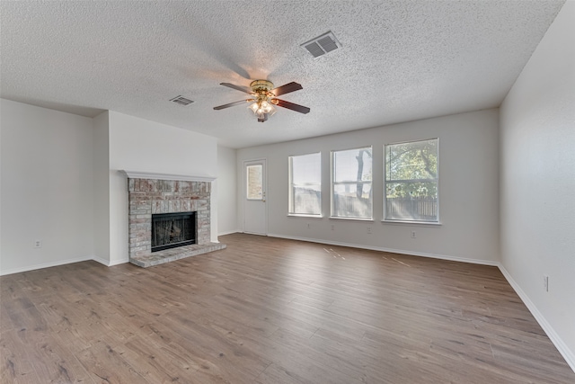 unfurnished living room featuring light hardwood / wood-style floors, ceiling fan, a fireplace, and a textured ceiling