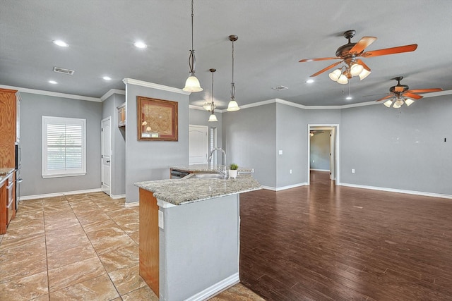 kitchen with sink, decorative light fixtures, a center island with sink, ornamental molding, and light stone countertops