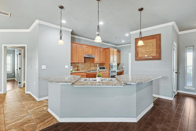 kitchen featuring light stone countertops, a kitchen island with sink, backsplash, and decorative light fixtures