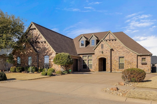 view of front of house featuring driveway, central air condition unit, a shingled roof, and brick siding