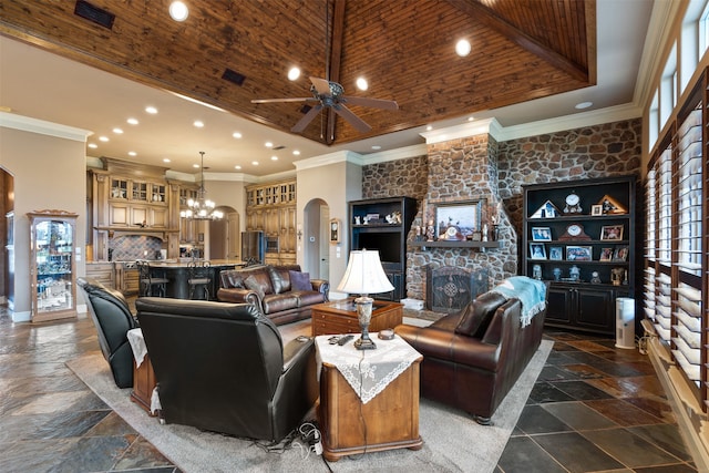 living room with a towering ceiling, ceiling fan with notable chandelier, a stone fireplace, wooden ceiling, and crown molding