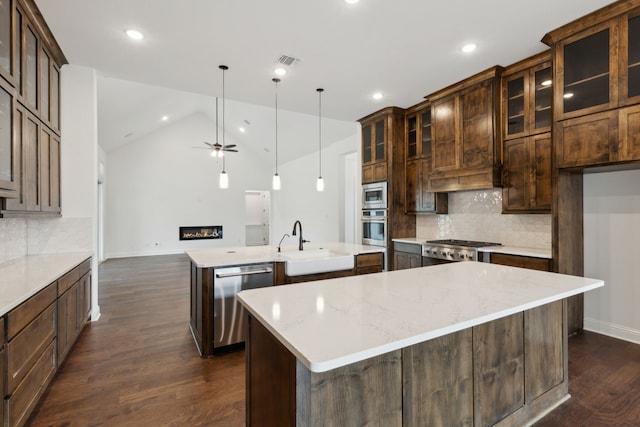 kitchen featuring light stone countertops, stainless steel appliances, a kitchen island with sink, sink, and pendant lighting