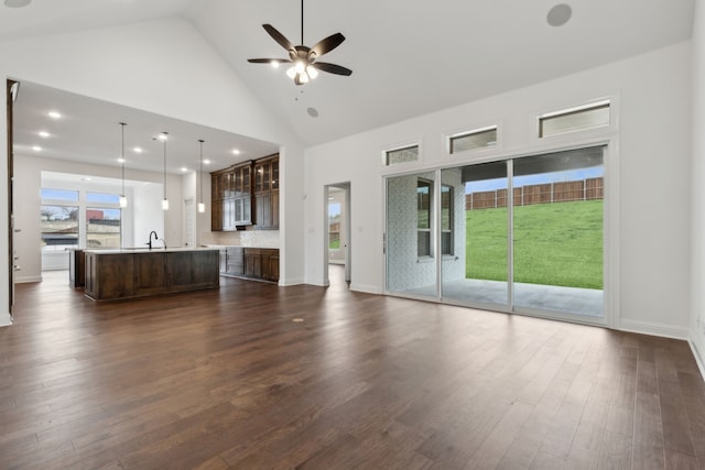 unfurnished living room with ceiling fan, sink, dark wood-type flooring, and high vaulted ceiling