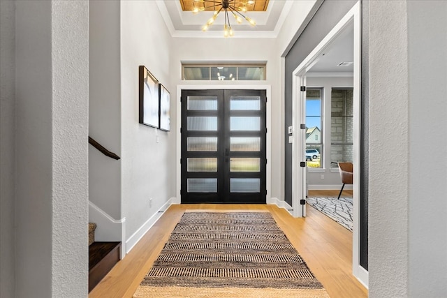 entrance foyer with a chandelier, light wood-type flooring, a tray ceiling, and crown molding