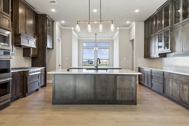 kitchen with a kitchen island with sink, backsplash, dark brown cabinets, and pendant lighting