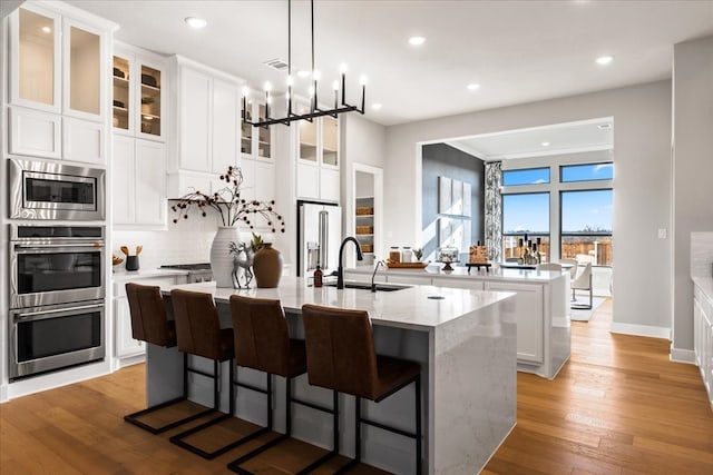 kitchen featuring white cabinetry, sink, stainless steel appliances, a breakfast bar, and a center island with sink