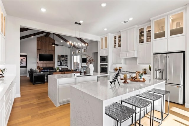 kitchen with a kitchen island with sink, hanging light fixtures, vaulted ceiling with beams, appliances with stainless steel finishes, and light hardwood / wood-style floors