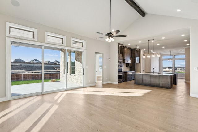 unfurnished living room with ceiling fan, sink, beamed ceiling, light hardwood / wood-style flooring, and a water view