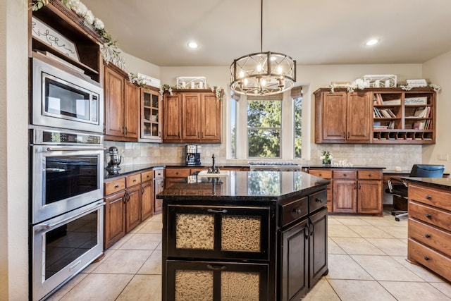 kitchen featuring backsplash, double oven, light tile patterned floors, a center island with sink, and an inviting chandelier