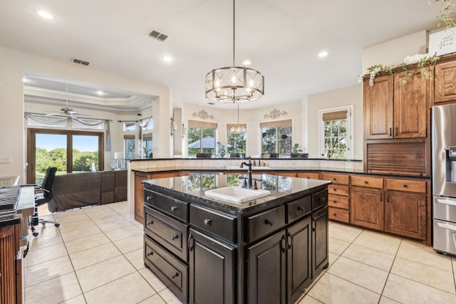 kitchen with sink, stainless steel refrigerator with ice dispenser, hanging light fixtures, light tile patterned floors, and an island with sink