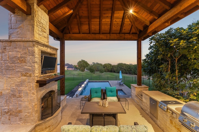 view of patio featuring a gazebo, an outdoor stone fireplace, a fenced in pool, and exterior kitchen