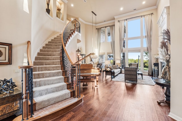 foyer entrance featuring wood-type flooring, crown molding, a wealth of natural light, and a towering ceiling