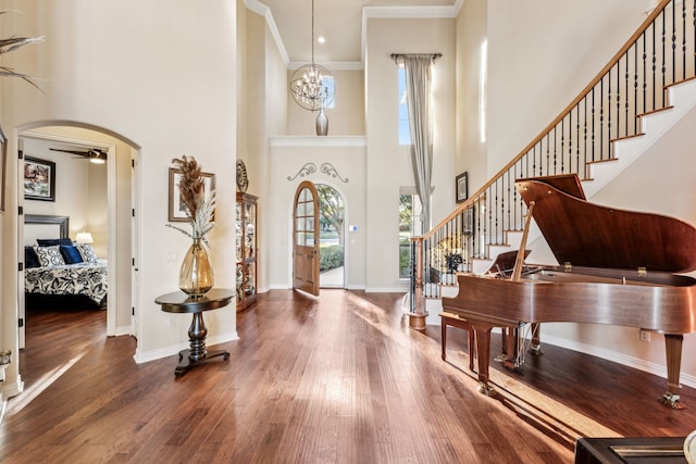 foyer with a towering ceiling, ornamental molding, a notable chandelier, and hardwood / wood-style flooring