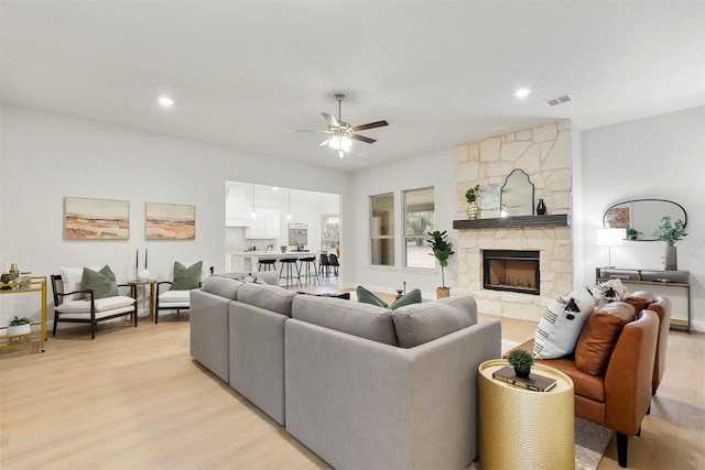 living room with a fireplace, ceiling fan, and light hardwood / wood-style flooring