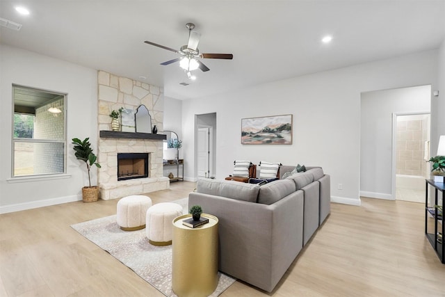 living room featuring ceiling fan, light hardwood / wood-style floors, and a stone fireplace