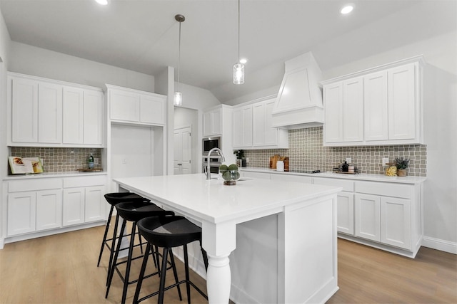 kitchen featuring white cabinets, custom range hood, a kitchen island with sink, and tasteful backsplash