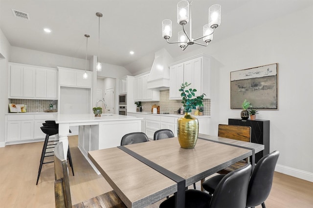 dining space featuring sink, an inviting chandelier, lofted ceiling, and light wood-type flooring