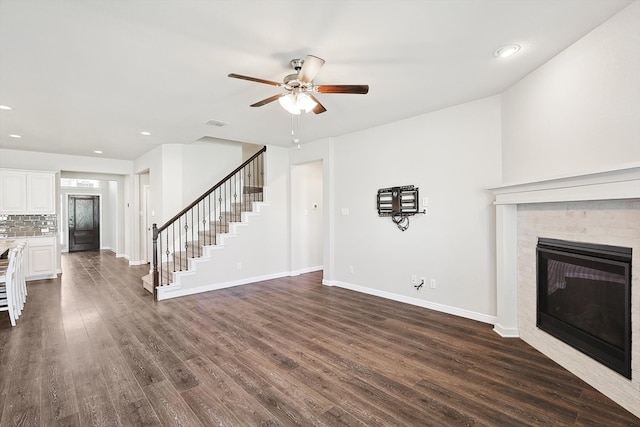 unfurnished living room with stairs, a ceiling fan, dark wood-style flooring, and baseboards