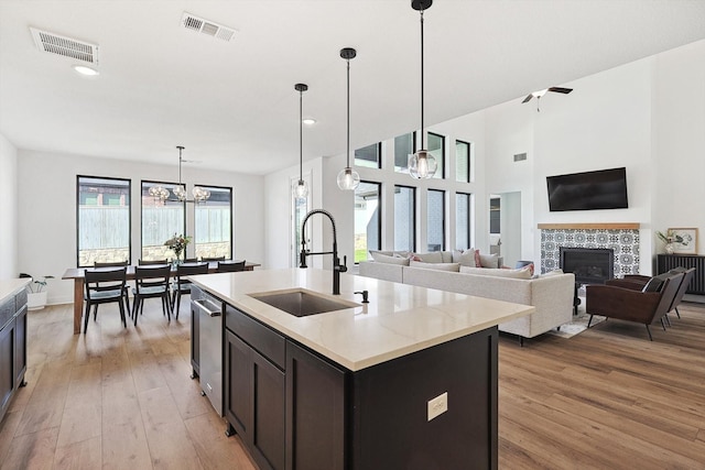 kitchen with light hardwood / wood-style floors, a center island with sink, decorative light fixtures, a fireplace, and sink