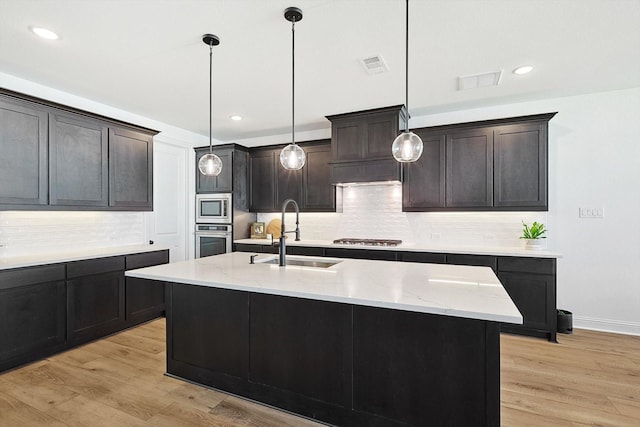 kitchen featuring stainless steel appliances, light hardwood / wood-style floors, a center island with sink, and sink