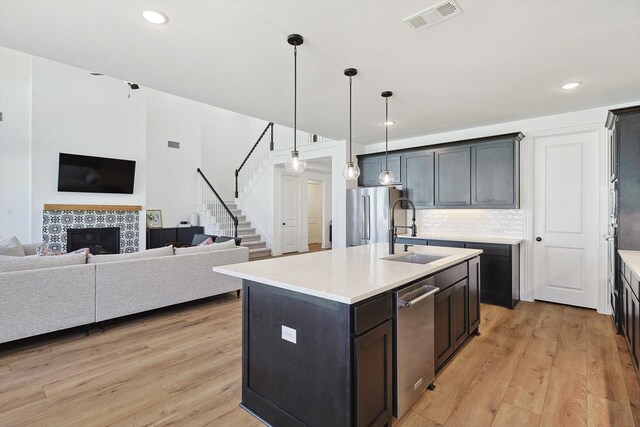 kitchen with an island with sink, stainless steel appliances, pendant lighting, a tile fireplace, and sink