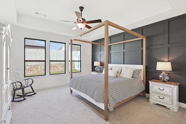 bedroom with ceiling fan, light colored carpet, and a tray ceiling