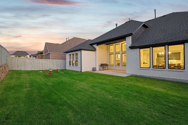 back house at dusk with a lawn and a patio area