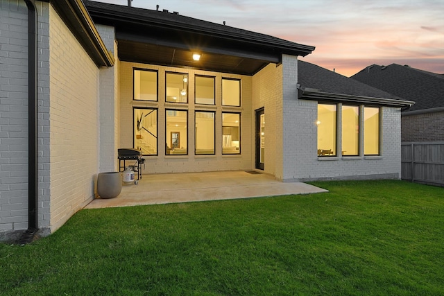 back house at dusk with a patio area and a yard