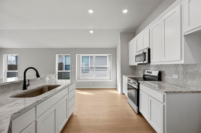 kitchen featuring appliances with stainless steel finishes, a wealth of natural light, white cabinets, light stone counters, and sink