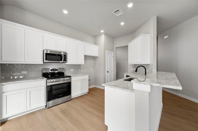 kitchen with white cabinets, stainless steel appliances, sink, kitchen peninsula, and light hardwood / wood-style flooring