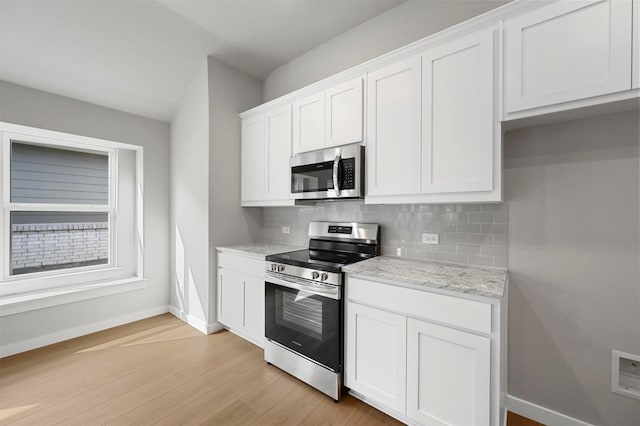 kitchen with white cabinetry, stainless steel appliances, backsplash, light wood-type flooring, and light stone countertops