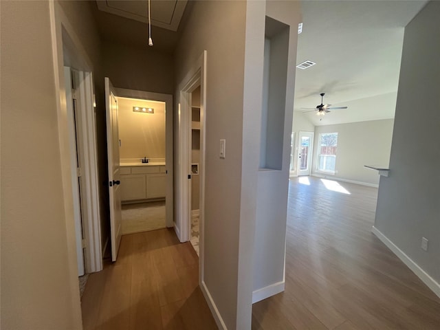 hallway with lofted ceiling, light wood-type flooring, and sink