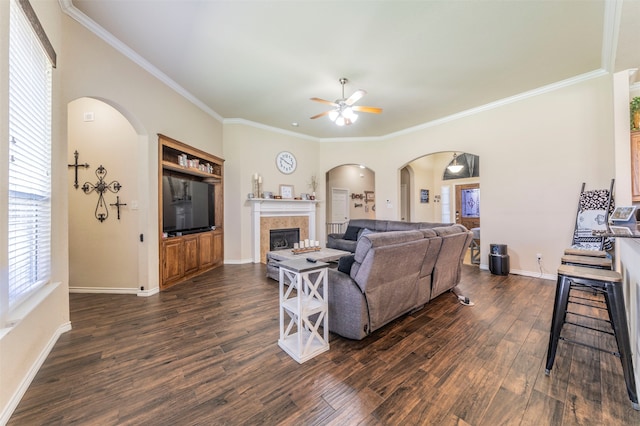 living room with dark hardwood / wood-style floors, ornamental molding, a tiled fireplace, and ceiling fan