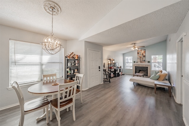 dining room featuring vaulted ceiling, ceiling fan with notable chandelier, a tiled fireplace, a textured ceiling, and wood-type flooring