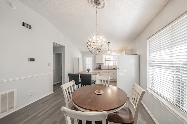 dining area featuring a textured ceiling, hardwood / wood-style flooring, sink, lofted ceiling, and an inviting chandelier