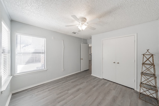 unfurnished bedroom featuring a textured ceiling, light hardwood / wood-style floors, ceiling fan, and a closet