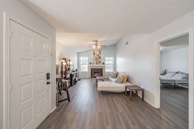 living room featuring vaulted ceiling, a tiled fireplace, a textured ceiling, ceiling fan, and hardwood / wood-style flooring