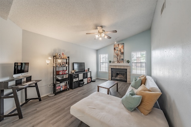 living room featuring ceiling fan, hardwood / wood-style floors, vaulted ceiling, and a tile fireplace